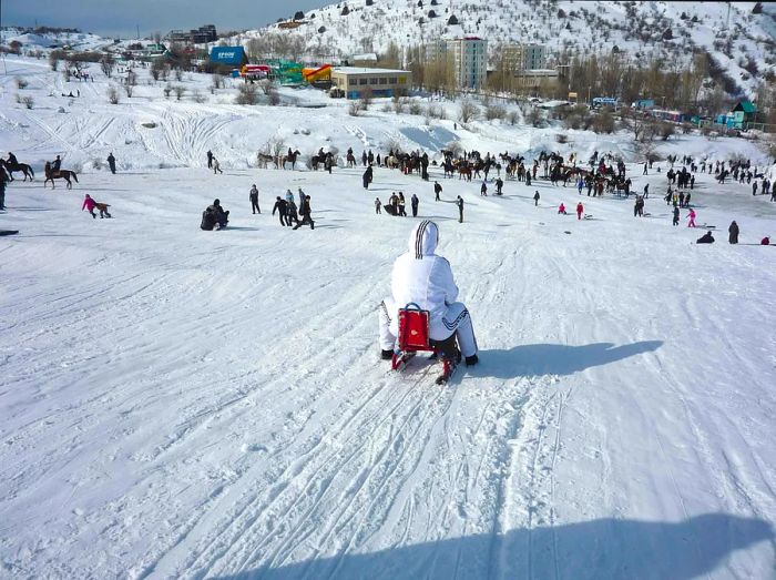 A child on a sled slides down a slope filled with people enjoying the snow