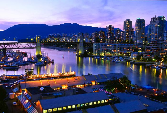 An Art Deco steel truss bridge spans False Creek, offering a pathway to the city skyline.