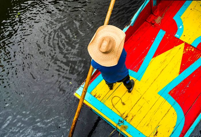 Aerial view of a person standing on a vibrant boat in a canal.