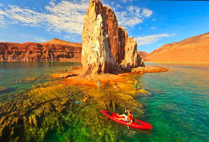 A man in a red canoe observing people on the shore of a rocky island.