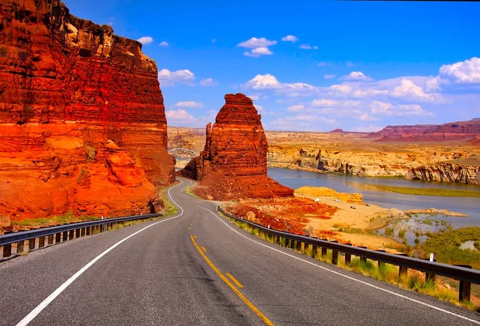 A deserted road winding through red and orange sandstone canyons with picturesque riverfront views.