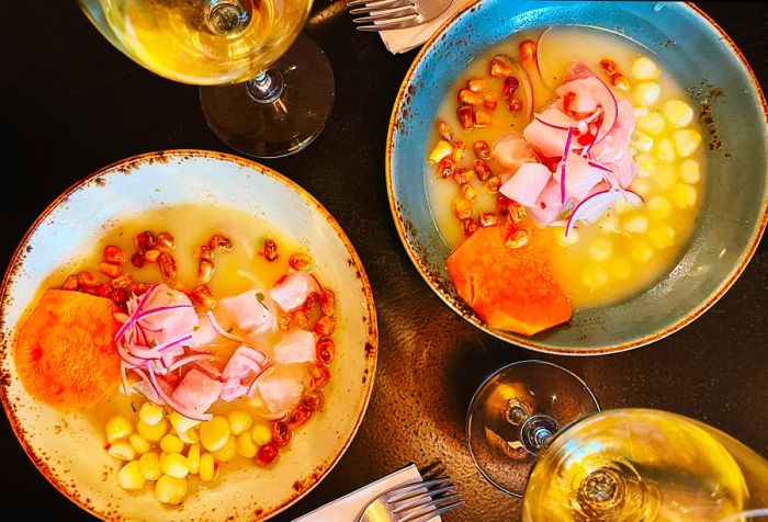 Two bowls of classic Peruvian ceviche accompanied by two glasses of wine.