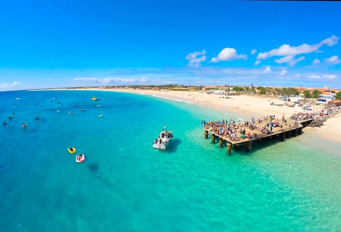 A bustling pier on a turquoise beach filled with floating boats.