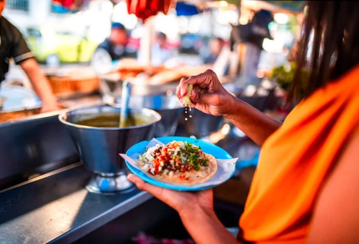 A person drizzles lemon juice over a platter of tacos they are holding.