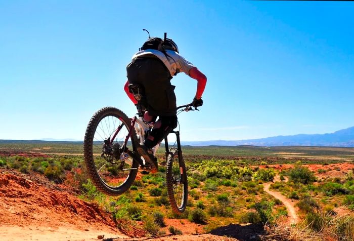 A man rides his bike with confidence across a wide, open, grassy landscape, enjoying the beauty of the clear blue sky above.