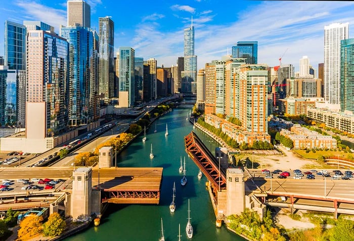 Aerial view of boats navigating a river surrounded by sleek, towering skyscrapers.