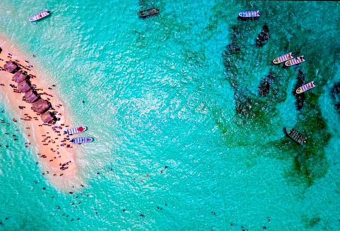 A slender sandbank embraced by turquoise waters, dotted with beach cottages and visitors basking in the lovely weather.