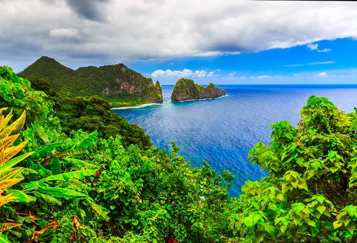 A lush, rocky island framed by the blue sea under a cloudy sky.