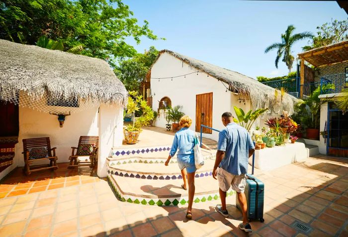 A couple strolling across the tiled floor of a resort, dragging their luggage behind them.