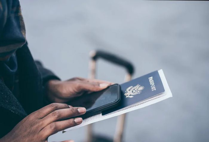 A young African American woman stands at the airport, holding her passport.