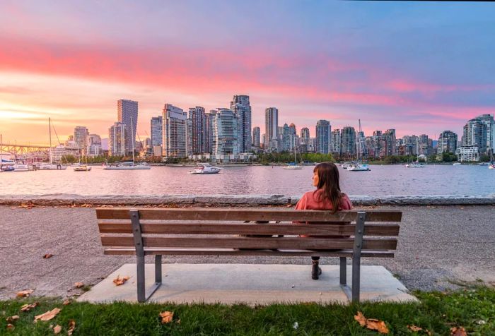 A woman relaxes on a bench overlooking a harbor filled with cruise boats, with the city skyline visible in the distance.