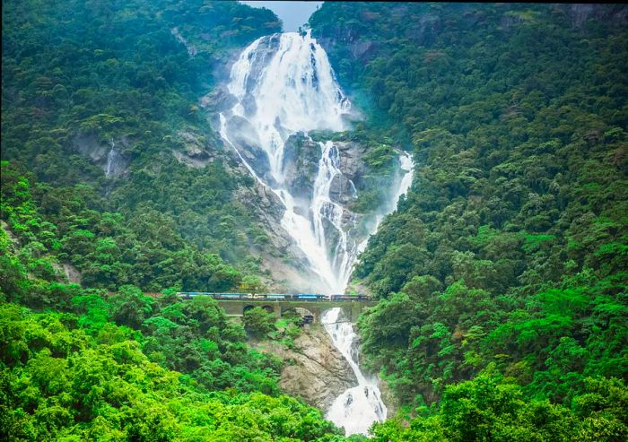 A Goa Express train glides past the stunning Dudhsagar Waterfall, Goa, India