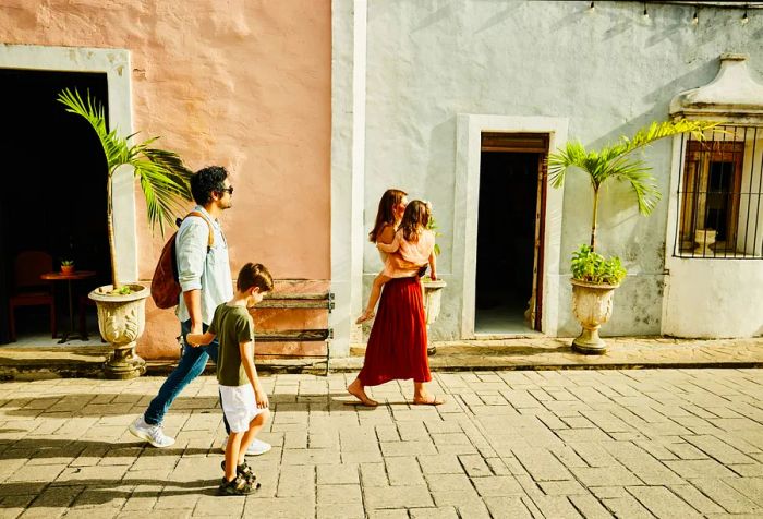 A family of four walks past a house on a residential street.