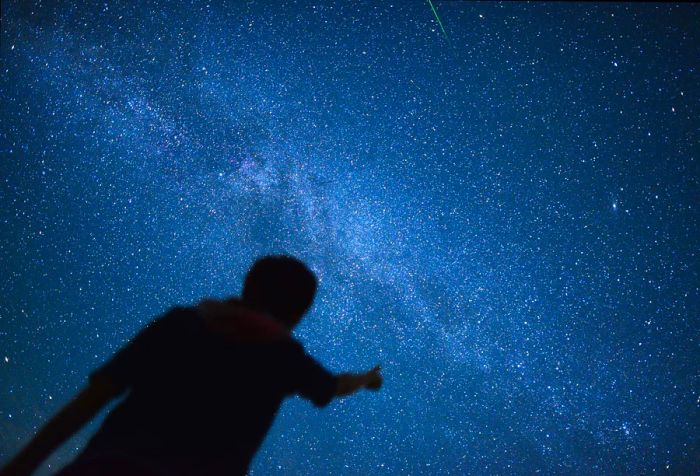 A silhouette of an individual gesturing toward a starry constellation.