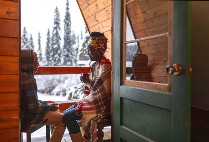 A mother and son relax on a small balcony, chatting with warm drinks in hand.