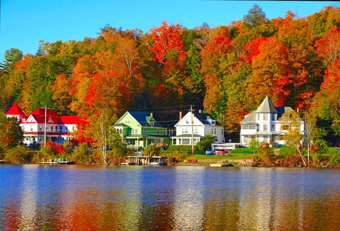 Charming Victorian-style homes line the lakeshore, shaded by tall trees adorned in vibrant autumn colors.