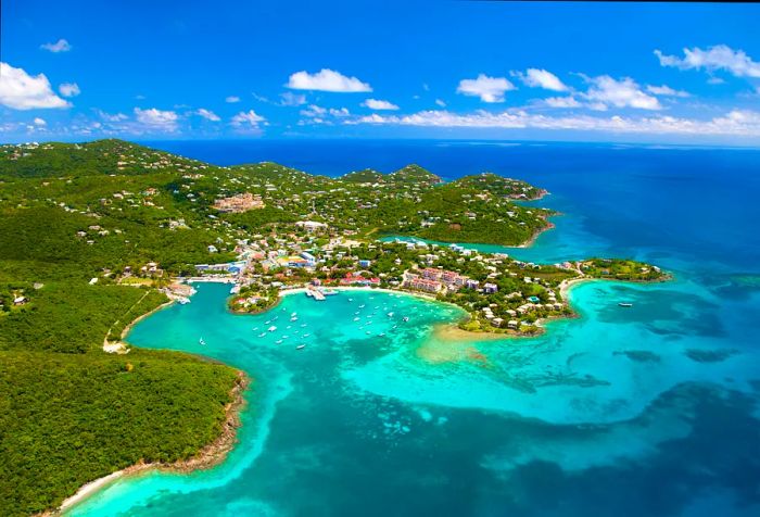 A charming coastal town with buildings nestled on forested hills overlooking a cove of turquoise waters.