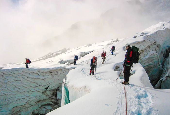 Hikers traverse the snowy slopes of the mountain on an overcast day.