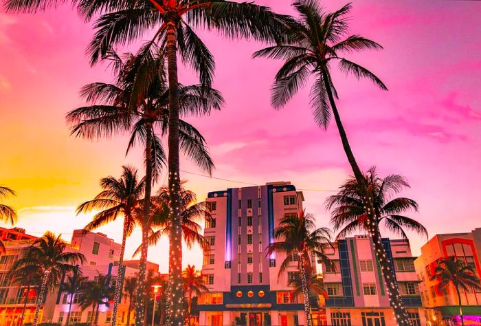 A line of mid-rise commercial buildings nestled among palm trees adorned with string lights beneath a pastel sky.