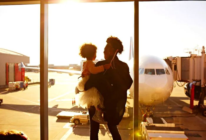 A mother and her daughter gaze at an aircraft from the terminal.