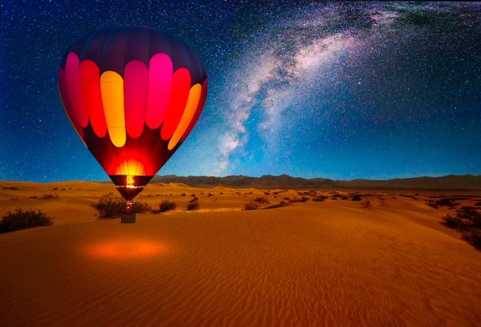 A stunning hot air balloon gracefully drifts beneath the starry Milky Way, floating peacefully over a vast desert expanse, creating an awe-inspiring nighttime tableau.