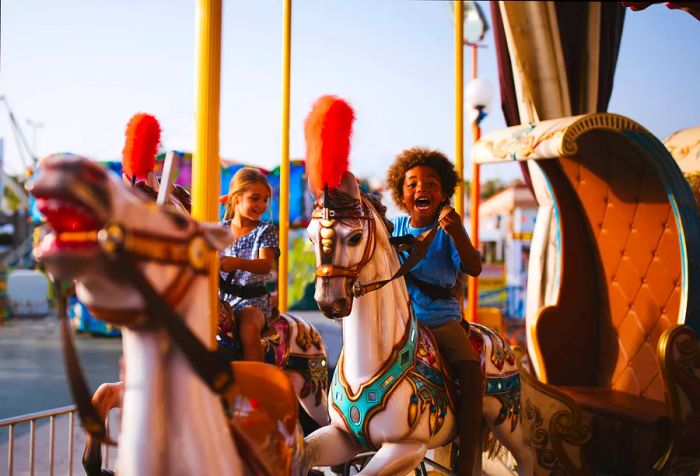 Two children delight in riding vibrant horse figures on a carousel.