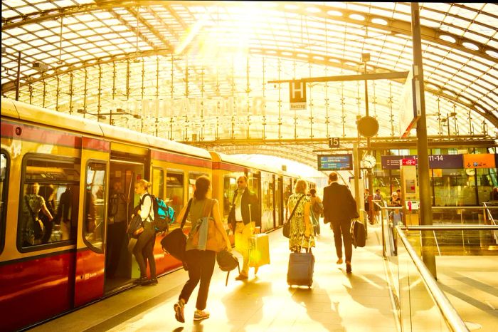 Travelers navigate through the modern Berlin Hauptbahnhof railway station, where an S-Bahn train awaits on the platform for boarding and disembarking.