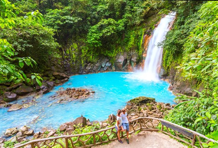 A couple of tourists admiring the Rio Celeste waterfall in Tenorio Volcano National Park, Guanacaste, Costa Rica.