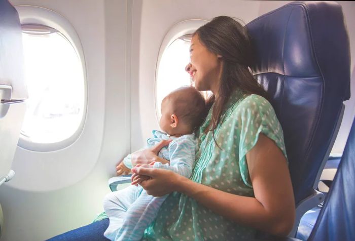 A mother and her baby sitting by the window on an airplane.