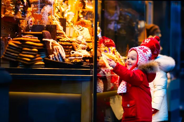 Children admiring pastries at a bakery in a traditional German Christmas market on a snowy winter day