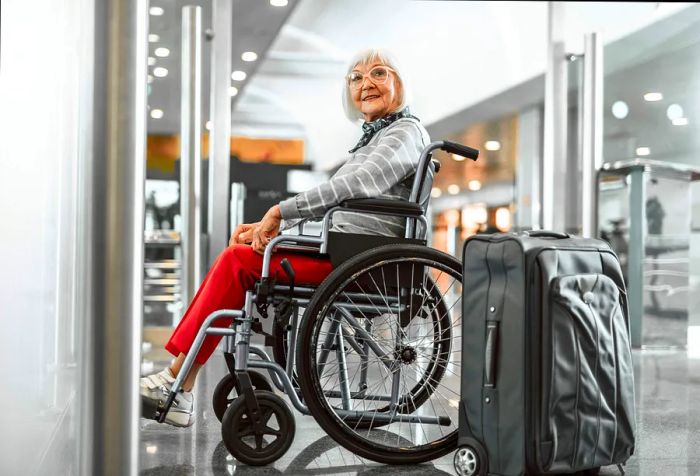 A full-length portrait of a mature woman sitting in a wheelchair at the airport, with a laptop and suitcase, waiting for her trip.