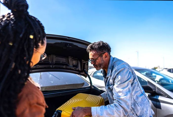 Friends retrieving luggage from the trunk of a car in the airport parking lot.