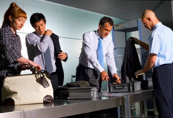 Three travelers navigate through airport security while an attendant inspects their belongings.