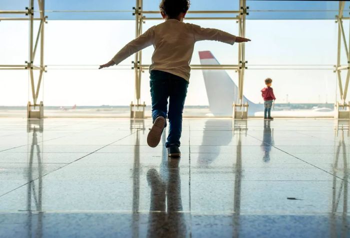 A boy standing on one foot while gazing at an airplane through the glass window in the airport.