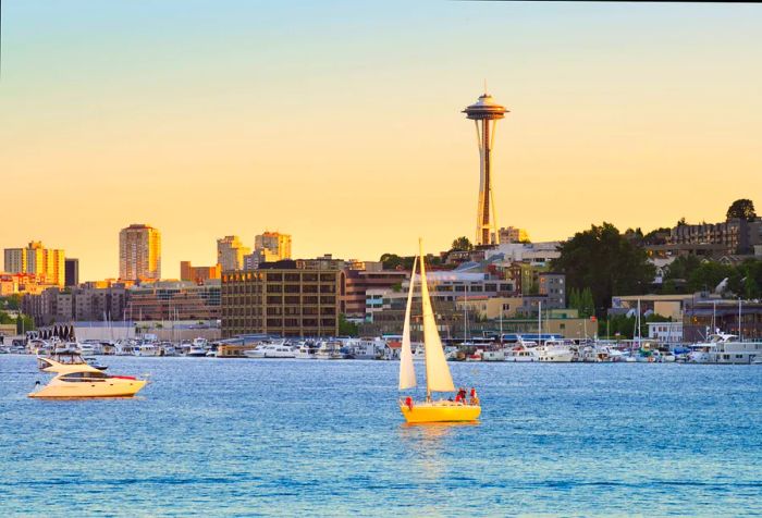 Boats gracefully glide across the serene surface of a peaceful lake, framed by a charming coastal town and a towering observation deck set against a stunning twilight sky.