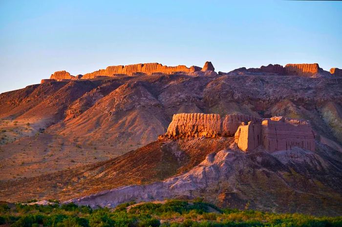 A red-stone medieval fortress ruins perched atop a cliff in a desert landscape