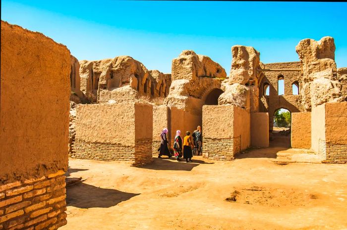 Visitors explore a crumbling structure with walls made of reddish mud.