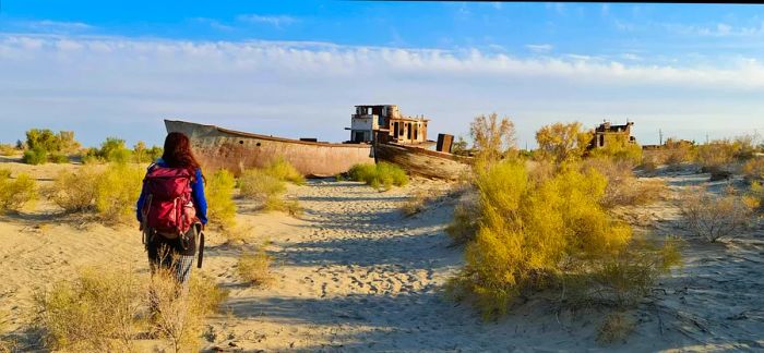 A woman walks among abandoned fishing trawlers and boats on the dry, sandy terrain that was once the bottom of the Aral Sea.