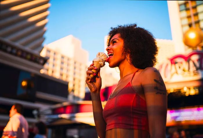 A joyful woman with a stunning afro enjoys ice cream while out in the city.