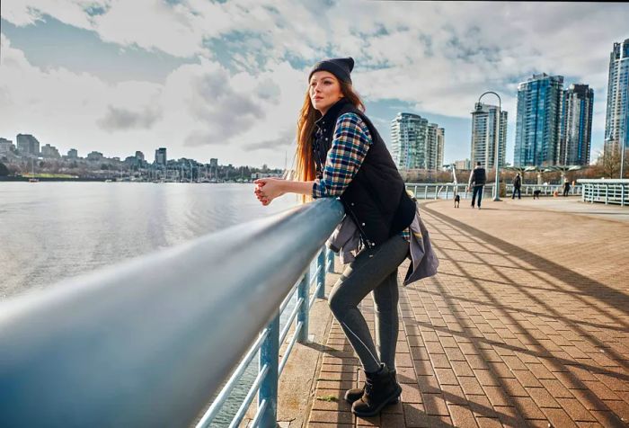 A young woman leans on the guardrail, thoughtfully watching the water while soaking in the peaceful ambiance of the promenade.