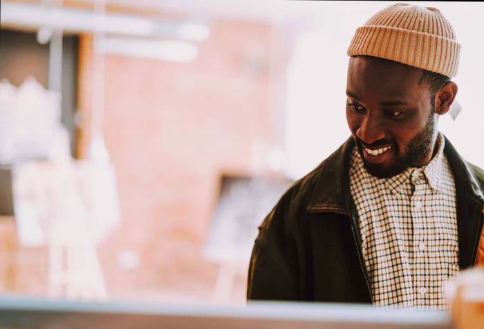 A joyful person gazes at something while donning a pink bonnet, jacket, and checkered shirt.