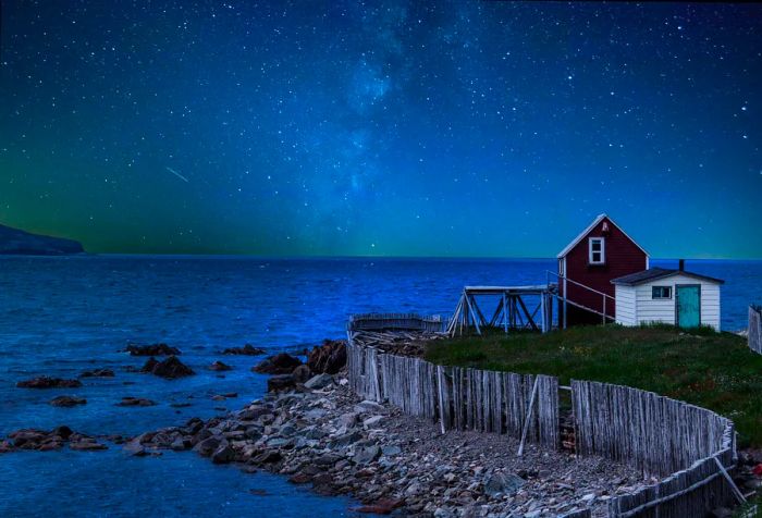 A quaint fishing hut perched over a dock by the beach at night, under a canopy of stars