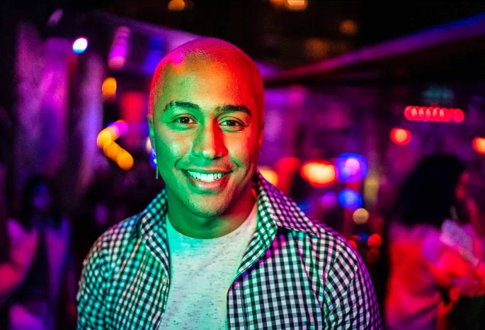 A portrait of a young bald man enjoying himself at a vibrant and colorful nightclub.