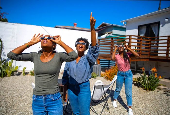 Female friends at home delighting in the solar eclipse while wearing eclipse glasses to safely view the sun.