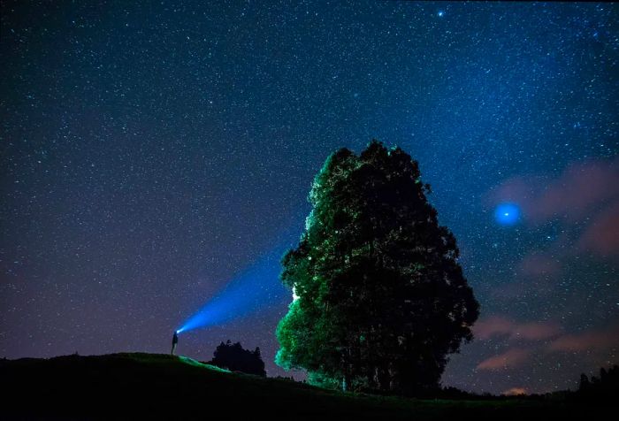 A night sky over the Azores, featuring a man with a flashlight illuminating a massive rock.