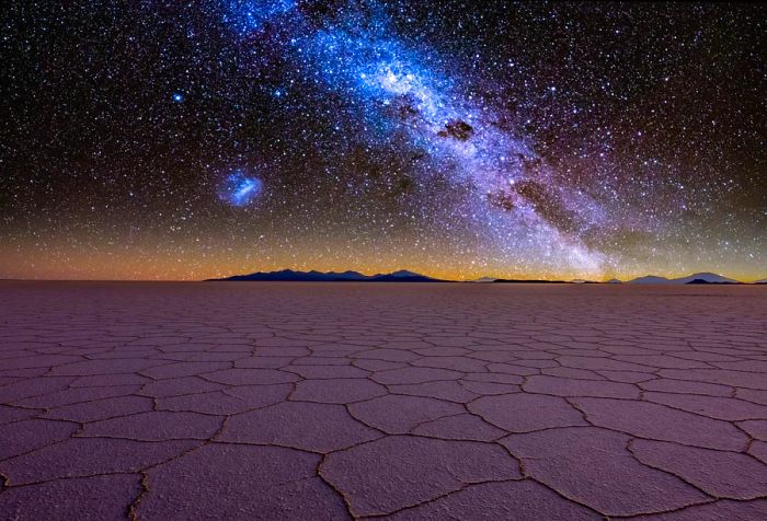 A vast salt flat illuminated by the Milky Way stretching across the starry night sky.