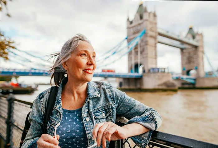 A senior woman rests against a fence with the iconic Tower Bridge in the background.