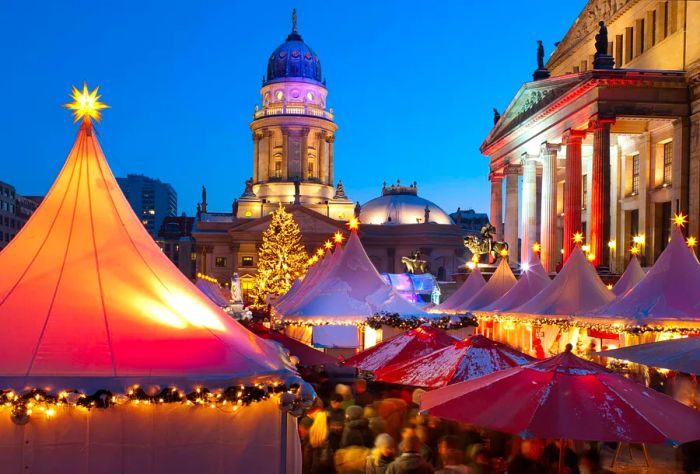 A church steeple overlooks a Christmas market filled with star-topped white tents.