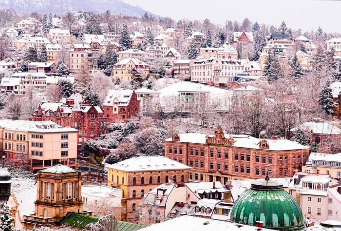 Aerial view of a snow-covered cityscape featuring historic buildings enveloped by tall, frost-laden trees.