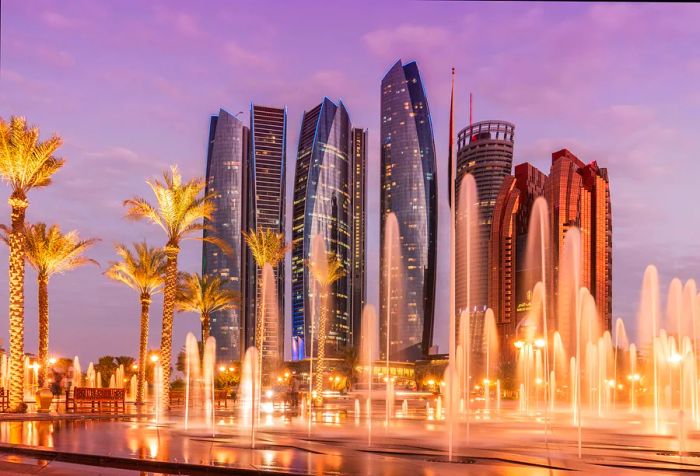 A stunning night scene featuring dancing fountains next to illuminated palm trees, with the city's skyscrapers in the background.